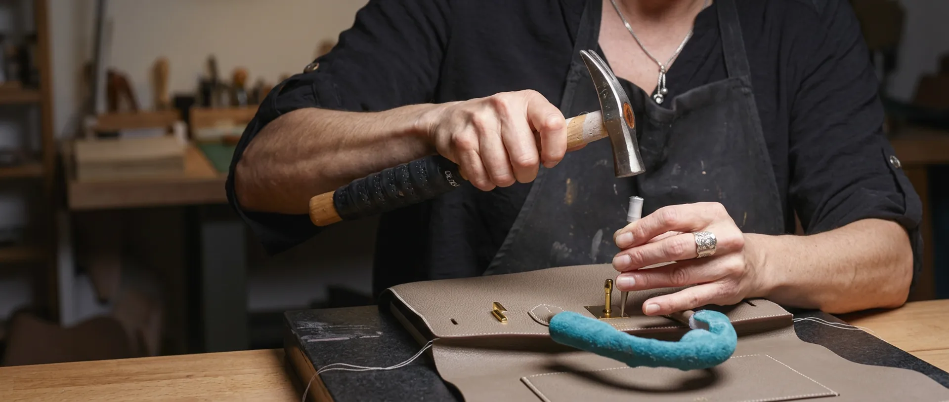 Craftsman hand-fitting gold hardware onto a taupe Hermès Birkin bag